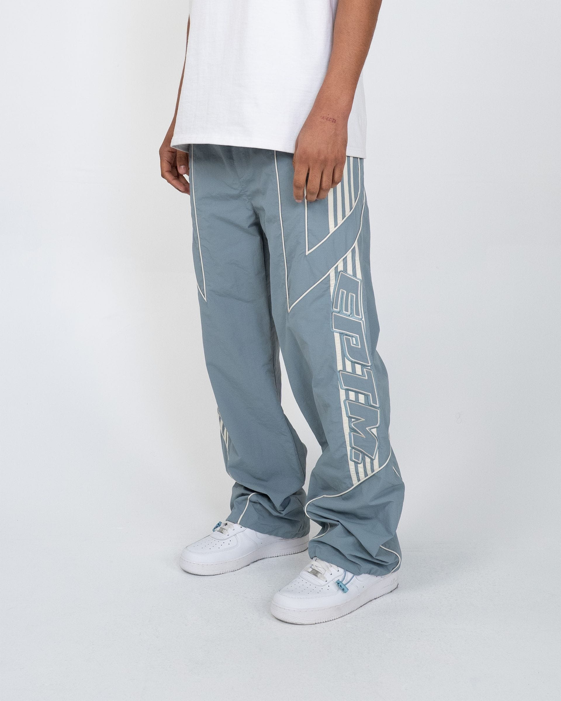 EPTM Pepe Track Pants in black, featuring a relaxed fit and elastic waistband, displayed on a hanger in the image.