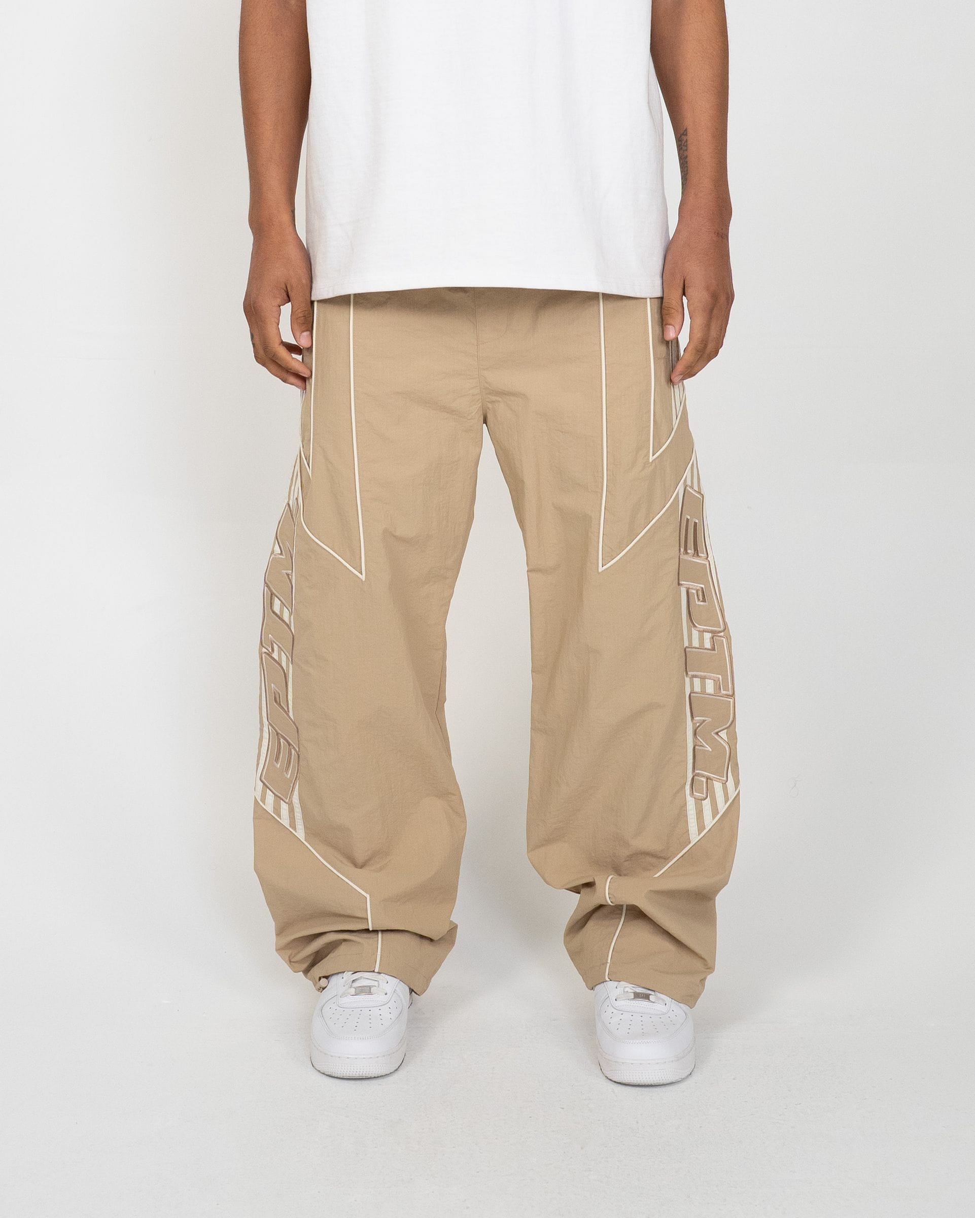 EPTM Pepe track pants in black fabric, featuring side stripes and relaxed fit, displayed on a hanger against a plain background.