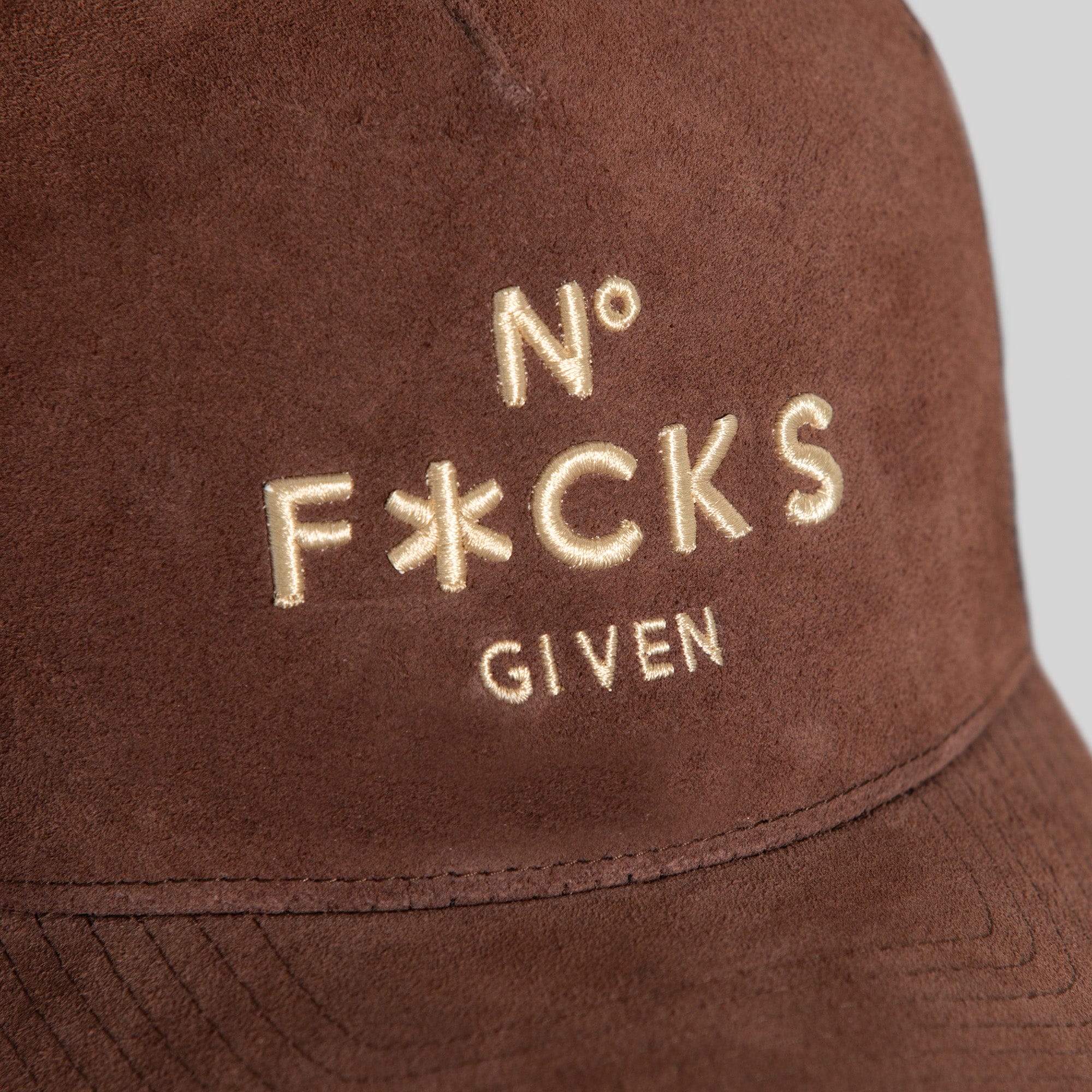 Field Grade No F*cks Given mocha suede mesh trucker hat with embroidered front and adjustable snapback closure.